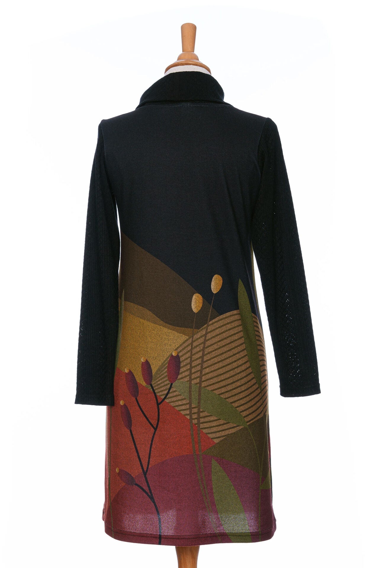 A back view of the Cornouiller Dress by Rien ne se Perd in Paysage print, featuring textured black fabric on the upper bodice and long sleeves and a landscape print on the body, with a cowl neck with a slit and coconut button detail, is shown on a mannequin in front of a white background.
