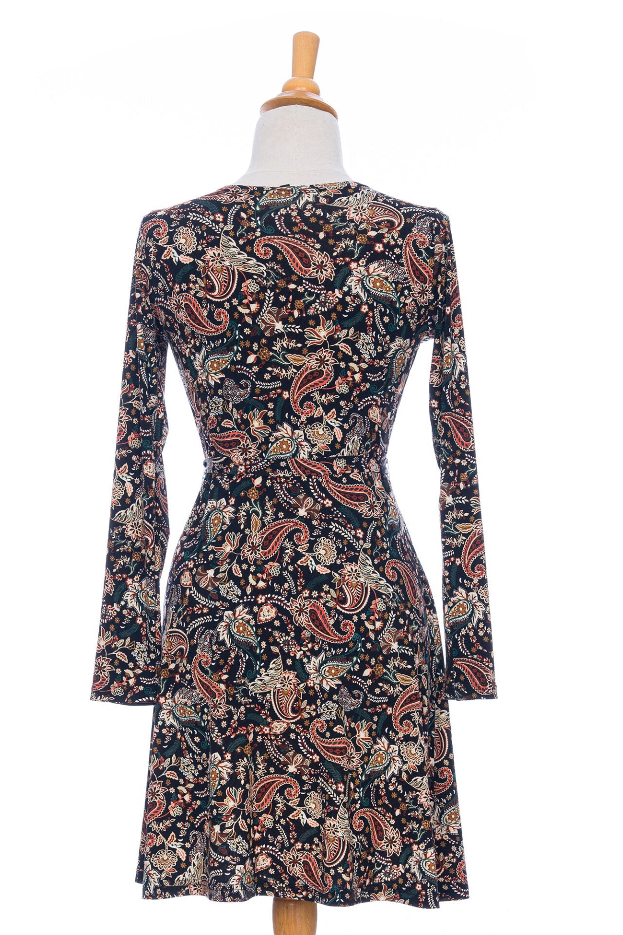 A back view of the Epilobe Dress by Rien ne se Perd in Fall Paisley, a classic wrap dress with a tie at the waist, delicate pleats at the shoulders, and a hem that hits above the knee, is shown on a mannequin in front of a white background. 