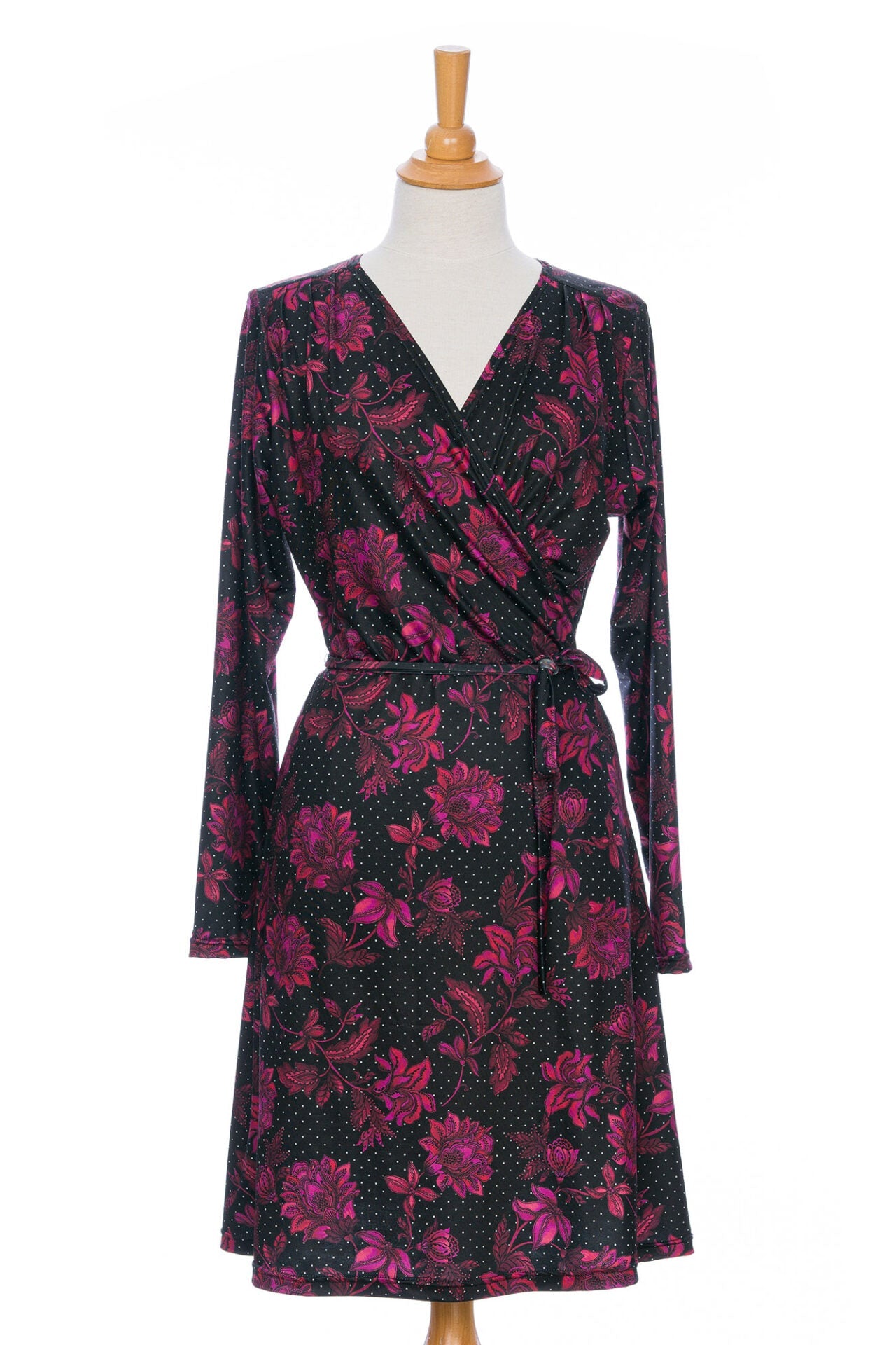 The Epilobe Dress by Rien ne se Perd in Polka Dots and Roses, a classic wrap dress with a tie at the waist, delicate pleats at the shoulders, and a hem that hits above the knee, is shown on a mannequin in front of a white background. 