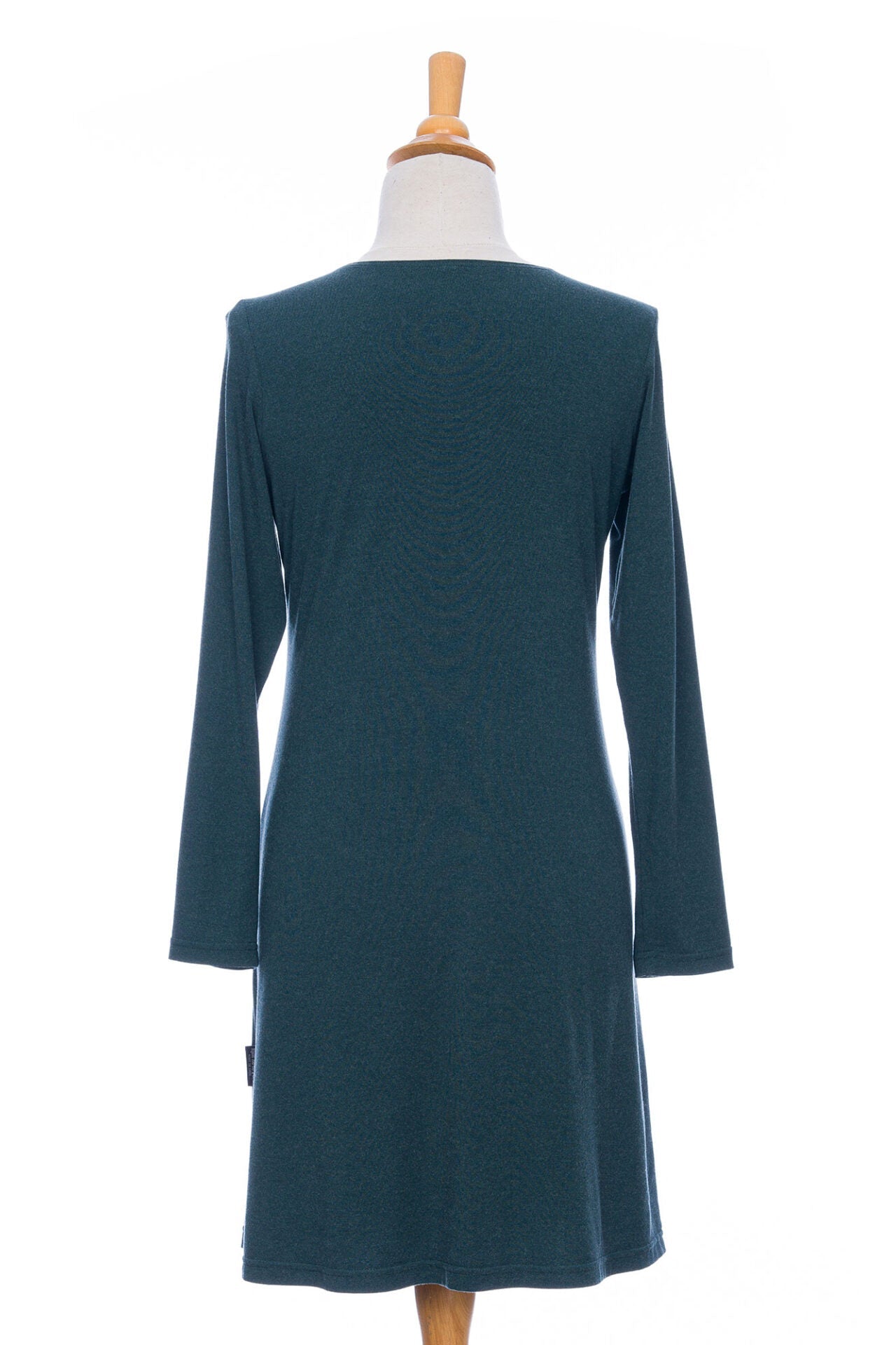 A back view of the Labrador Dress by Rien ne se Perd in Emerald, a semi-fitted dress with a v-neck, long sleeves, tie detail at the side waist, and above the knee length, is shown on a mannequin in front of a white background. 