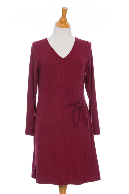 The Labrador Dress by Rien ne se Perd in Garnet, a semi-fitted dress with a v-neck, long sleeves, tie detail at the side waist, and above the knee length, is shown on a mannequin in front of a white background. 