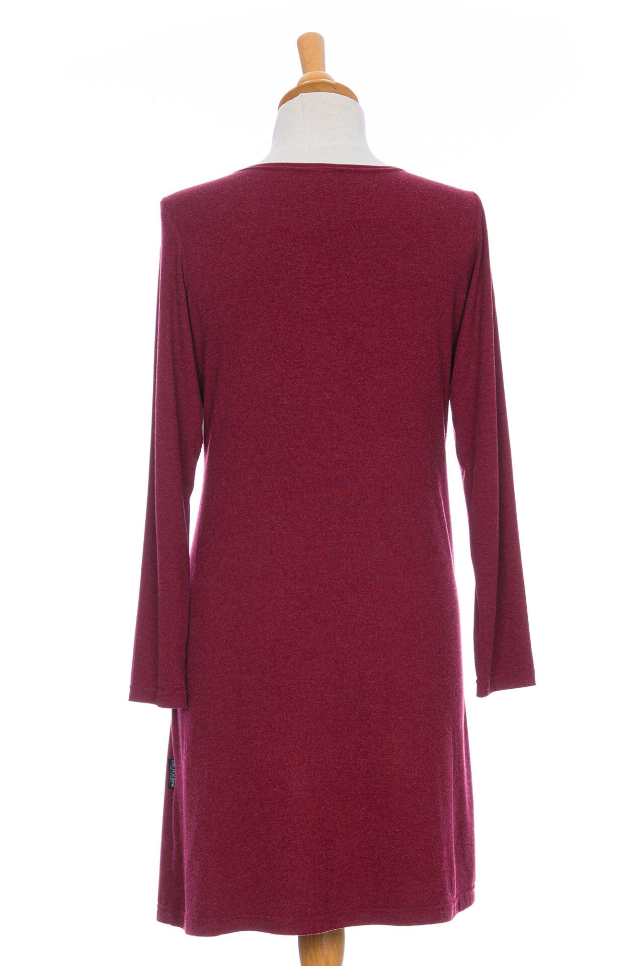 A back view of the Labrador Dress by Rien ne se Perd in Garnet, a semi-fitted dress with a v-neck, long sleeves, tie detail at the side waist, and above the knee length, is shown on a mannequin in front of a white background. 