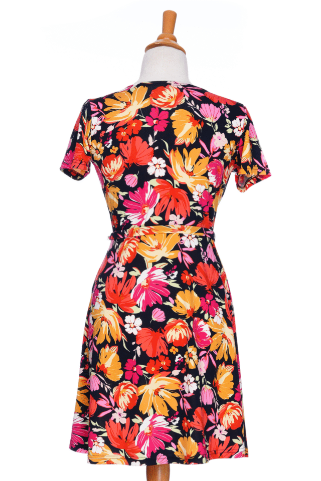 A back view of the Margarita Dress by Rien ne se Perd in Red/Orange floral print, with a faux wrap neckline, short sleeves, and short a-line skirt, is shown on a mannequin in front of a white background.