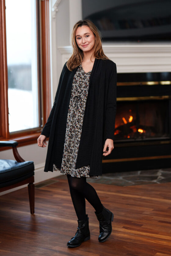 A woman wearing the Riopelle Dress by Rien ne se Perd in a Small Flowers print, standing in front of a fireplace