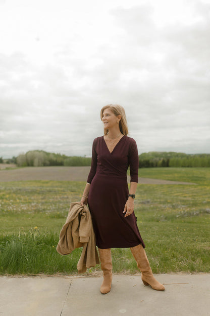 A woman wearing the St-Laurent Dress by Rien ne se Perd in Porto, a midi-length wrap style dress with a 3/4 sleeves and subtle shoulder pleats. She is standing outdoors.
