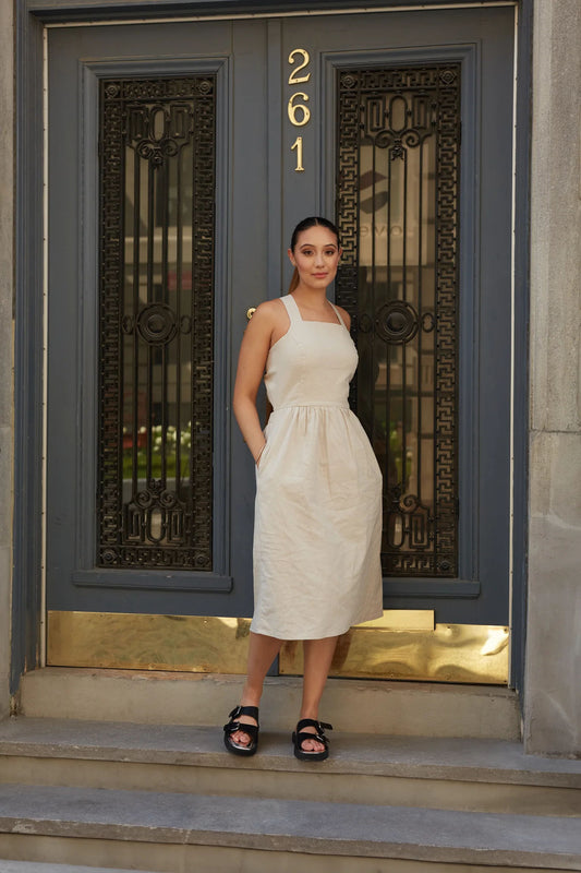 A woman wearing  the Santorini Dress by MAS in Oat, standing in front of an ornate doorway