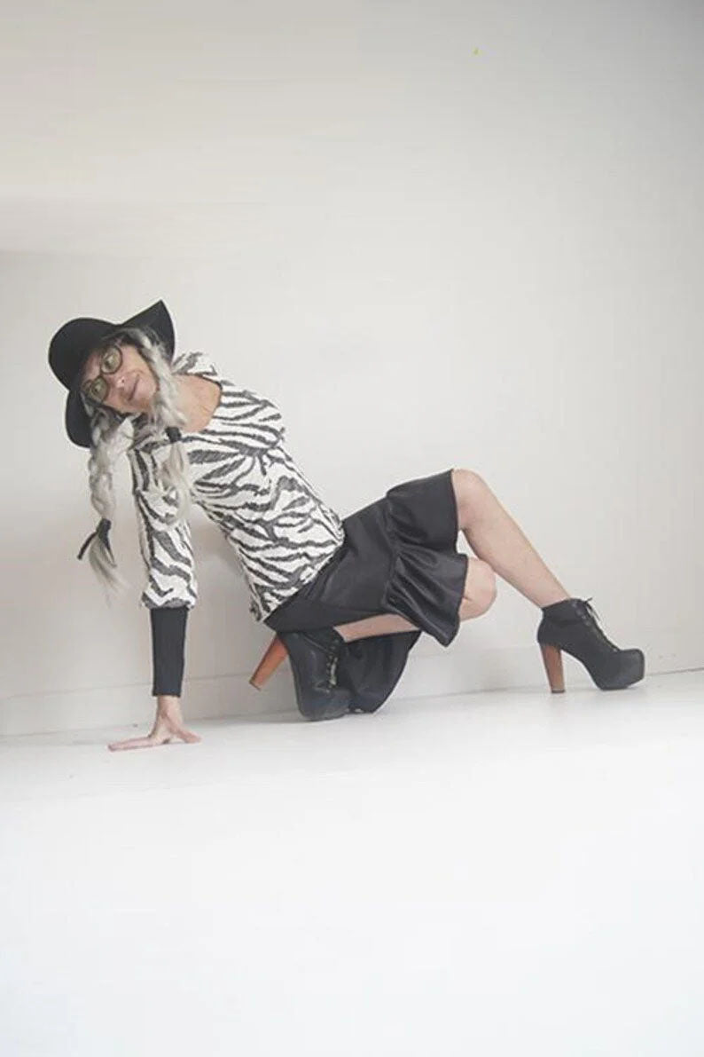 A woman wearing the Athena Top by SI Design in Black/White, with a square neckline, and empire waist, and bishop style sleeves with long cuffs in black lace. She is wearing it with a black skirt and is posing in front of a white background 