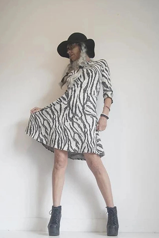 A woman wearing the Casual Dress by SI Design in Ivory/Black, with a round neck, 3/4 sleeves, a loose fitting A-line shape, and a knee length, posing in front of a w white background 