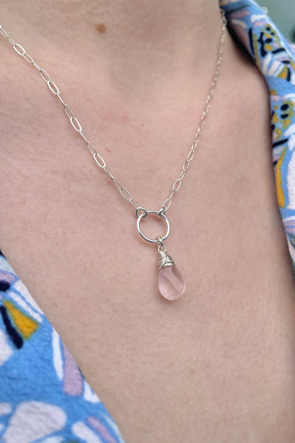 Necklace with a teardrop-shaped pink crystal pendant worn by a person in a patterned garment.
