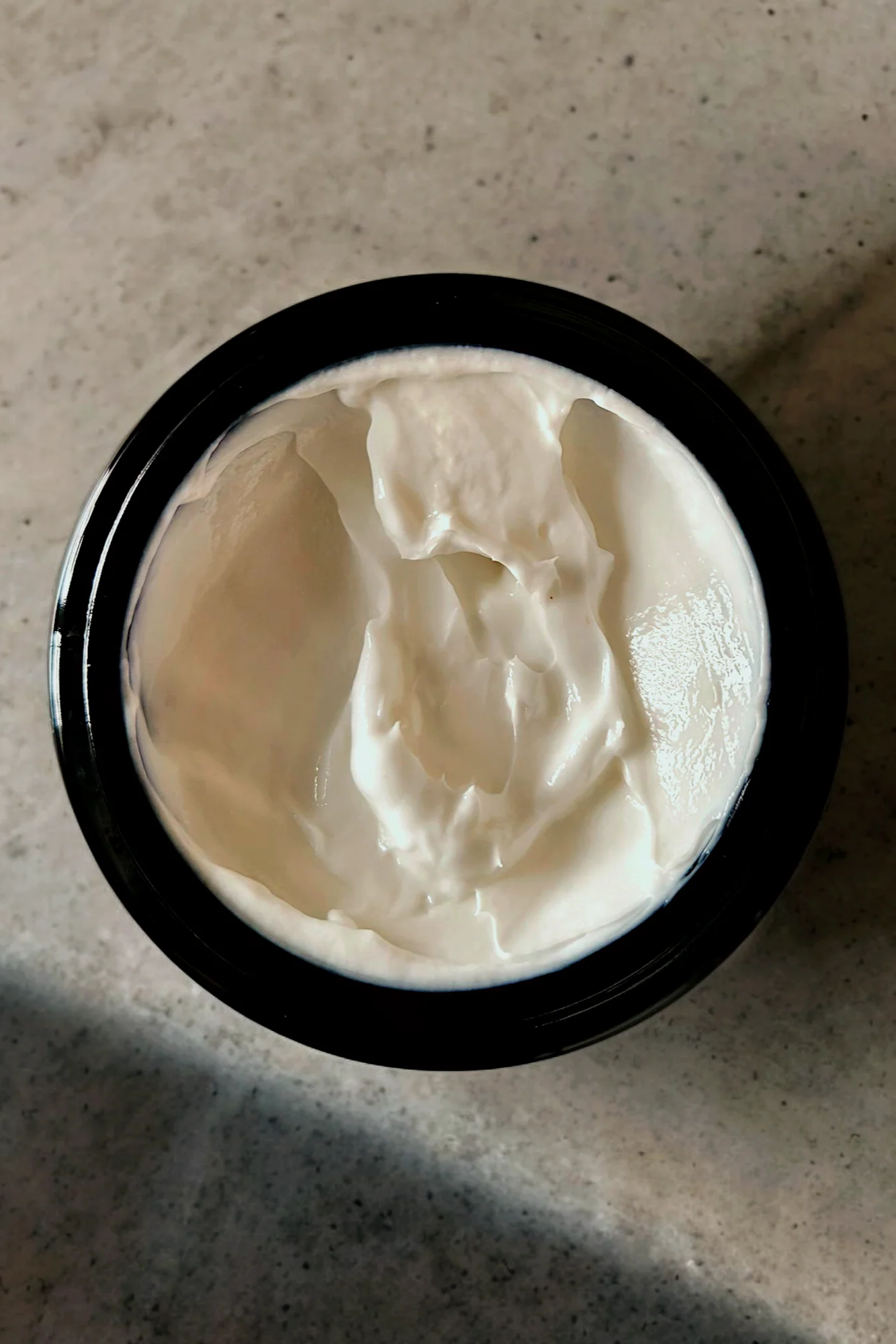 A open jar of 'Calming chamomile' face cream by Stay Wild Apothecary is shown on stone surface 