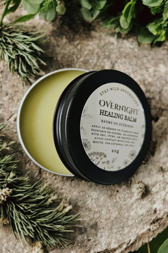 An 'Overnight Healing Balm' container by Stay Wild Apothecary is shown on a stone surface with natural elements