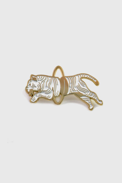 The Tiger Pin from Badaboöm studio, showing a split white and gold tiger leaping through a golden hoop, is shown against a white background. 