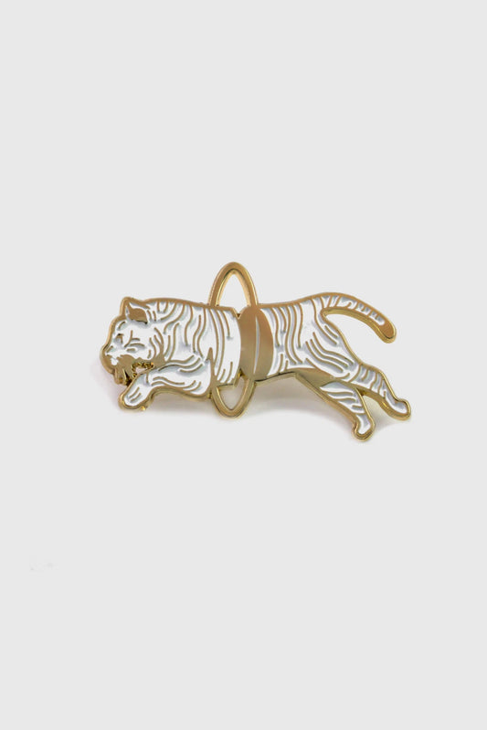 The Tiger Pin from Badaboöm studio, showing a split white and gold tiger leaping through a golden hoop, is shown against a white background. 