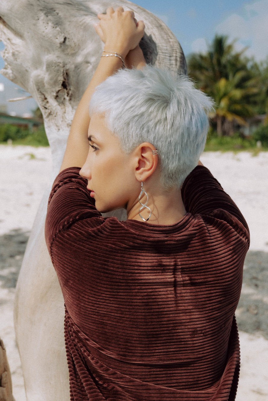 Back view of a woman wearing the Tofino T-Shirt by MAS in Cacao, a short sleeved top in ribbed velvet. She is standing on a beach.