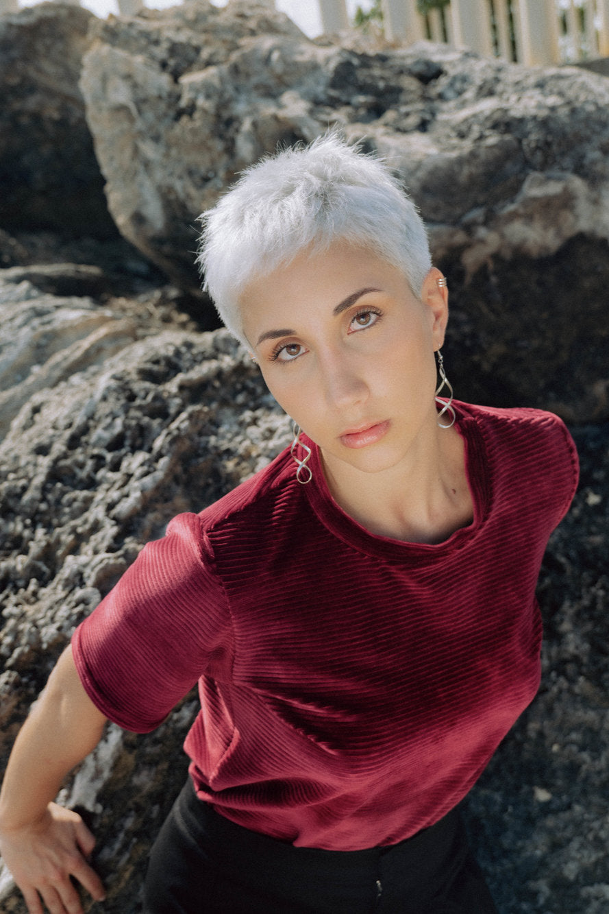 A woman wearing the Tofino T-Shirt in Rosewood by MAS, a short sleeved top in ribbed velvet. She is standing in front of boulders.