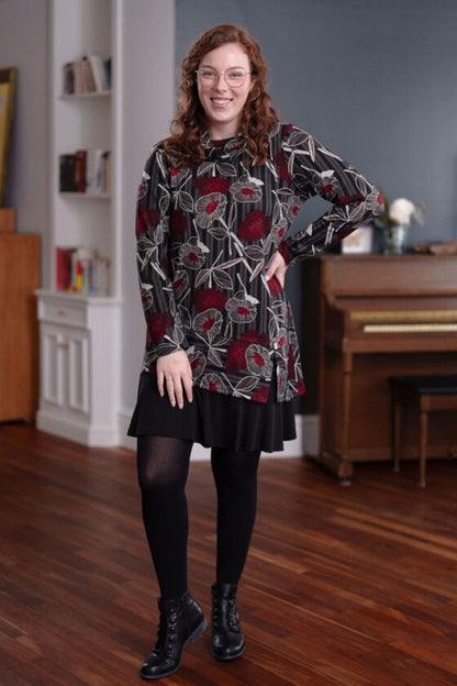 A woman wearing the Corno Tunic by Rien ne se Perd in Black and Red with a black skirt stands in front of a piano. 