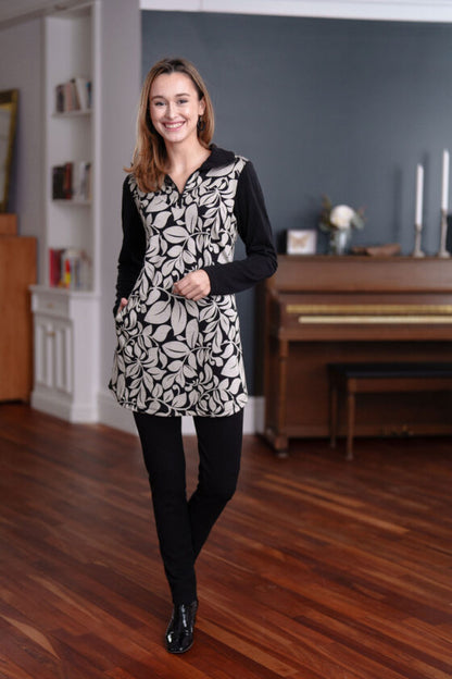 A woman wearing the Marcelle Tunic by Rien ne se Perd in Foliage Black and White with black pants stands in front of a piano.