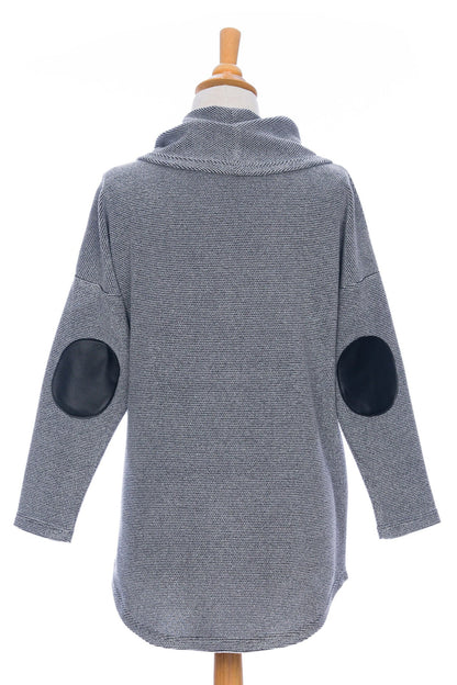 Back view of the Myrique Tunic by Rien ne se Perd in Grey, an oversized chenille tunic with a large cowl neck, rounded hem, faux leather elbow patches, button placket at the left shoulder, and patch pocket on the front, is shown on a mannequin in front of a white background. 