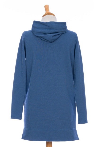 A back view of the Toundra Tunic by Rien ne se Perd in Blue, featuring a large hood with drawstrings, a kangaroo pocket, and a relaxed fit, is shown on a mannequin in front of a white background. 