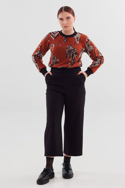 A woman wearing the Wanda Sweater in Tiger print by Slak with black pants, standing in front of a white background 