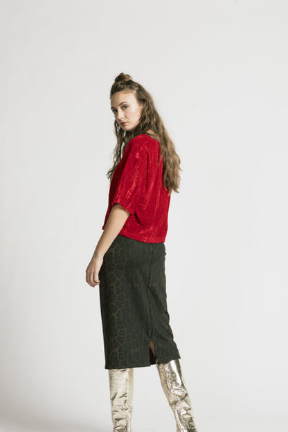 Back view of woman wearing the Wuthering Top by Allison Wonderland in red crushed velvet, with a dark skirt, standing in front of a white background 