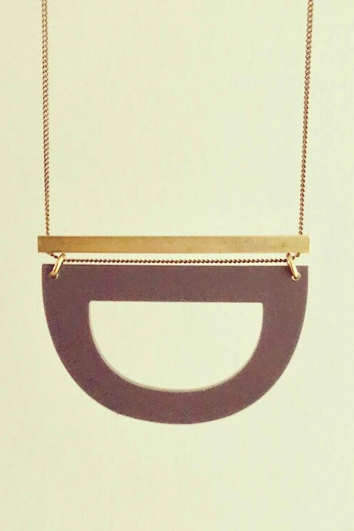 Luppe long necklace by Darlings of Denmark; solid brass horizontal bar and acrylic hollowed out half circle; hanging flat lay